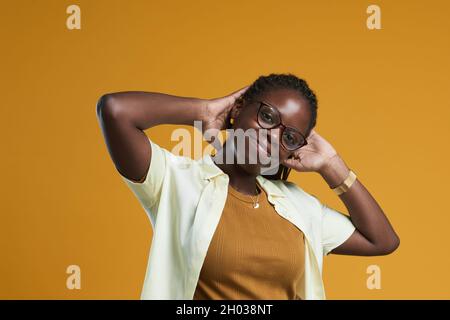 Porträt einer sorglosen afroamerikanischen Frau, die auf die Kamera schaut und lächelt, während sie vor gelbem Hintergrund im Studio posiert, Kopierraum Stockfoto