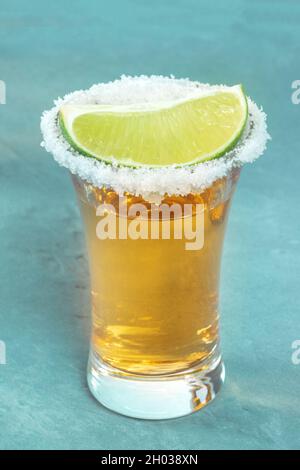 Goldener Tequila, mit einem Salzrand und einer Limettenscheibe, Nahaufnahme aus einem Winkel auf blauem Hintergrund Stockfoto