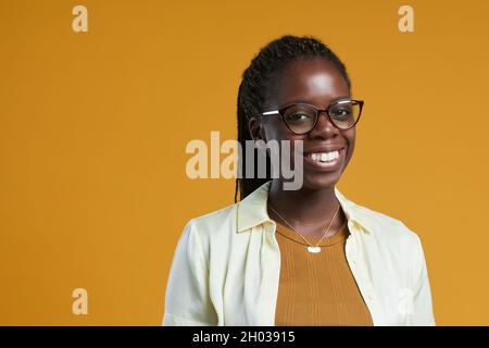 Porträt einer jungen afroamerikanischen Frau, die eine Brille trägt und die Kamera anlächelt, während sie vor gelbem Hintergrund im Studio posiert, im Kopierraum Stockfoto