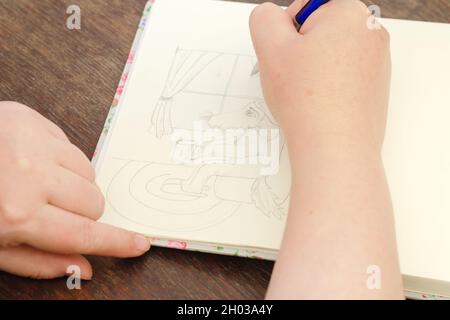 Eine Frau zeichnet eine Bleistiftzeichnung eines Hundes mit einer Tasse Kaffee. Das Haustier sitzt auf einem Stuhl. Öffnen Sie das Notizbuch auf einem braunen Holztisch. Teil einer Serie. Se Stockfoto