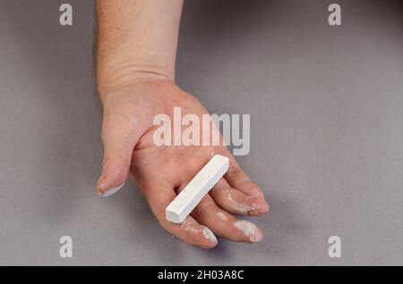 Ein Stück weiße Kreide liegt vor grauem Hintergrund in der Hand des Mannes. Der Mann hält ein rechteckiges Stück Kreide in seiner offenen Handfläche. Selektiver Fokus. Stockfoto