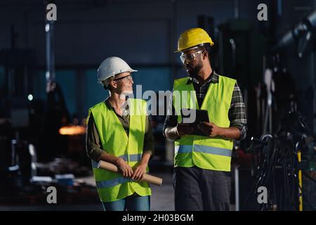 Porträt von Industrieinspektoren mit Tablet, die eine allgemeine Überprüfung durchführen und in Innenräumen in einer Metallwerkstatt sprechen. Stockfoto