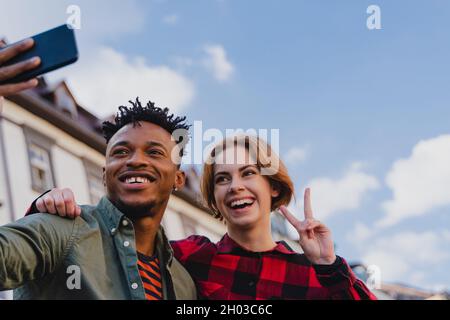Low-Angle-Ansicht des jungen Biracial Paar macht Selfie für soziale Netzwerke im Freien in der Stadt. Stockfoto