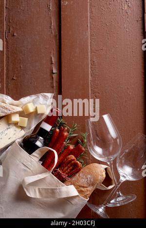 Draufsicht auf Baguette und Flasche Rotwein auf Holztisch mit Weinläsern und Käse Stockfoto
