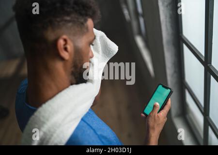 Mit dem Smartphone kann man den jungen afroamerikanischen Sportler im Fitnessstudio aus der Perspektive betrachten. Stockfoto