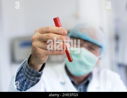 Nahaufnahme des Hand haltenden Reagenzrohrs des Forschers mit roter Flüssigkeit im Labor Stockfoto