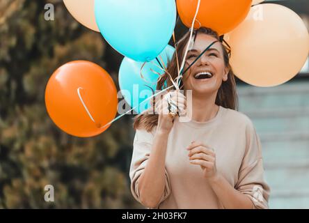 Portrait einer netten fröhlichen Frau mit bunten Luftballons, die Spaß im Freien haben. Genießen Sie Geburtstagsfeier in warmen sonnigen Tag auf dem Garten. Stockfoto