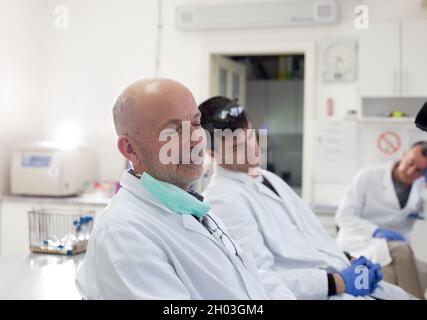 Müde Techniker in weißen Mänteln und mit Handschuhen, die im Labor einschlafen Stockfoto