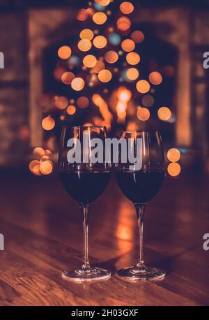 Zwei Gläser Rotwein auf festlicher Bokeh-Hintergrund. Romantischer Abend in der Nähe von Christmas Tree at Home. Elegante Neujahrskarte. Stockfoto