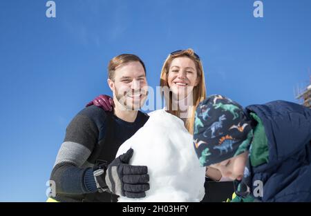 Eltern mit Kind spielen auf Schnee, machen Schneemann. Familienurlaub im Winter Stockfoto