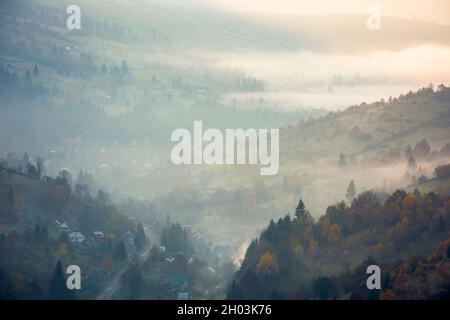 Landschaft Berglandschaft an einem nebligen Morgen. Schöne Naturlandschaft mit Bäumen in bunten Laub auf den Hügeln und Dorf im fernen val Stockfoto