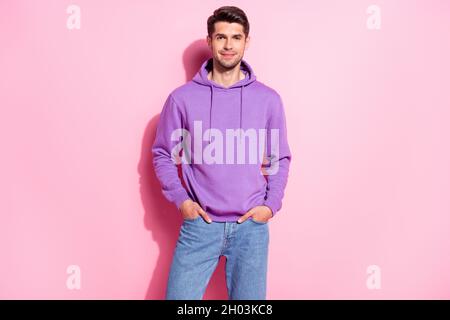 Portrait von attraktiven fröhlichen Inhalt Kerl trägt komfortablen Hoodie Hände in Taschen isoliert über rosa Pastellfarben Hintergrund Stockfoto