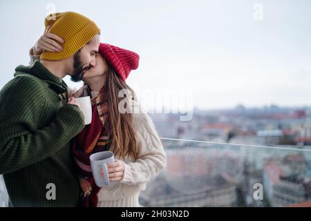 Junges Paar mit Kaffee stehen und küssen im Freien auf dem Balkon mit Blick auf die Stadt Stockfoto
