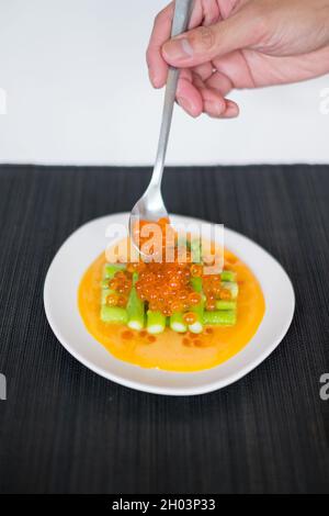 Hand legt roten Lachs-Kaviar auf Mini-Spargel mit Sauce auf weißem Teller im japanischen Restaurant, Nahaufnahme, flaches Lay, Bild für die Speisekarte, gesundes Essen Stockfoto