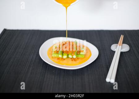 Gießt Sauce von Hand auf Minispargel mit rotem Kaviar. Weißer Teller und Essstäbchen auf schwarzer Matte im japanischen Restaurant, Nahaufnahme, Bild für die Speisekarte Stockfoto