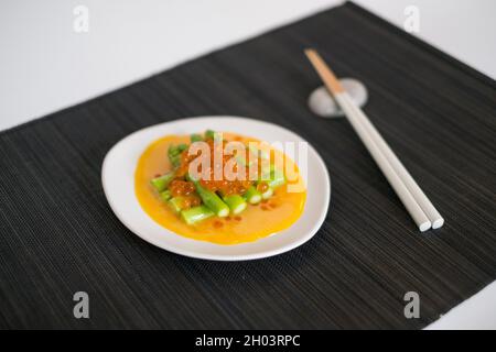 Mini-Spargel mit Sauce und rotem Kaviar auf weißem Teller mit Essstäbchen auf schwarzer Matte im japanischen Restaurant, Nahaufnahme, flaches Lay, Bild für die Speisekarte Stockfoto