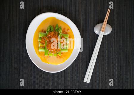 Mini-Spargel mit Sauce und rotem Kaviar auf weißem Teller mit Essstäbchen auf schwarzer Matte im japanischen Restaurant, Nahaufnahme, flaches Lay, Bild für die Speisekarte Stockfoto