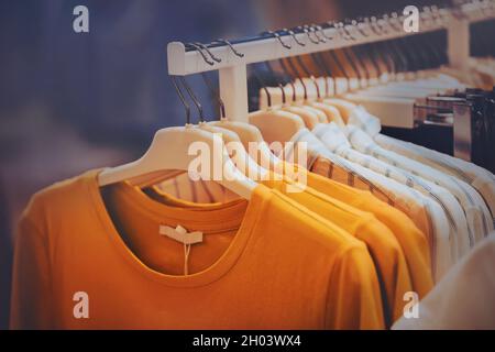 Modische Freizeitkleidung – gelbe Langarm- und gestreifte Hemden – hängen im Laden an Kleiderbügeln. Kleidung im Einkaufszentrum kaufen. Einkaufen. Stockfoto