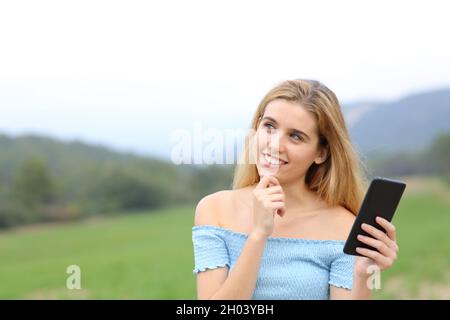 Fröhlicher Teenager, der Smartphone hält und sich wundert, draußen auf einem Feld zur Seite zu schauen Stockfoto