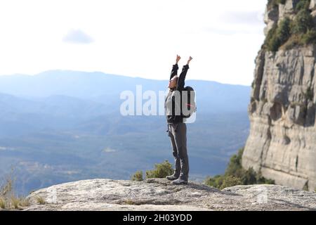 Profil eines Wanderers, der die Arme in einer Klippe hebt Stockfoto