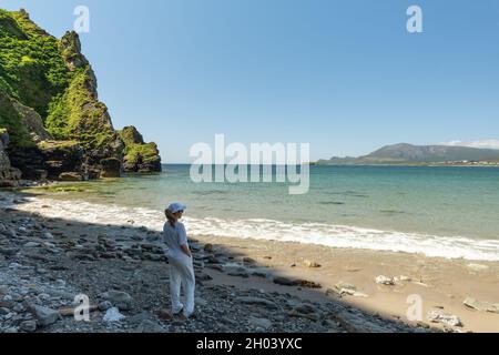 Aufnahme einer jungen Frau in Weiß, die vom Keel Beach auf Achill Island, Irland, aus den Ozean blickt Stockfoto