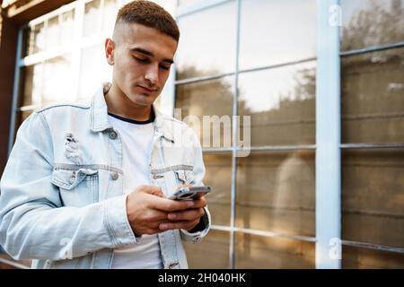 Junger zwangloser Mann in der Stadt, der Smartphone benutzt, während er auf der Straße läuft Stockfoto