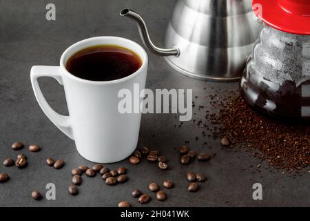 Eine Tasse Kaffee und die dritte Generation gießen über die Kaffeemaschine auf dem Steinboden Stockfoto