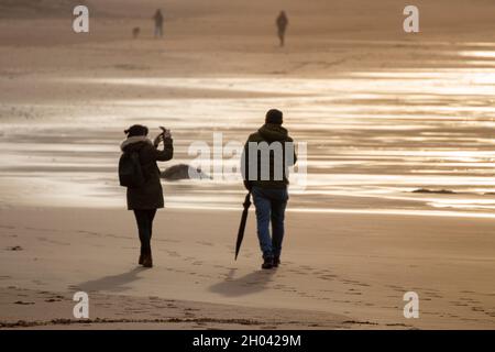 Frau, die an einem Wintertag am Strand bei Sonnenuntergang Bilder von einem Mann fotografiert Stockfoto