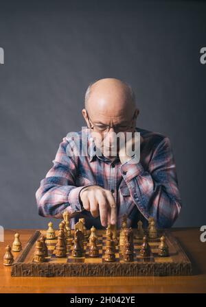 Alter Mann spielt Schach im Zimmer mit grauem Hintergrund Stockfoto