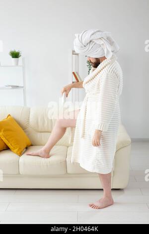 Lustiger bärtiger Mann reibt Körpercreme auf seine Beine. Spa-, Körper- und Hautpflege für den Mann Konzept Stockfoto