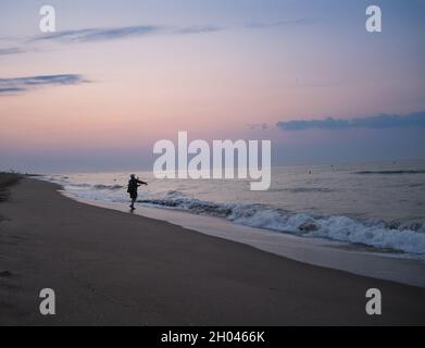 Ein Mann fischt bei Sonnenaufgang mit seiner Rute am Strand. Stockfoto