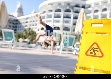 Junger Mann, der in der Nähe des gelben Warnschildes auf rutschige Fliesen fällt Stockfoto