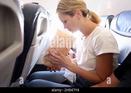 Junge Frau, die im Flugzeug fliegt und in einen Papiersack atmet Stockfoto