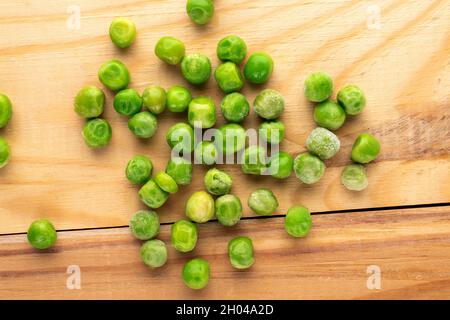 Mehrere gefrorene grüne Erbsen, Nahaufnahme, auf einem weißen Holztisch, Draufsicht. Stockfoto