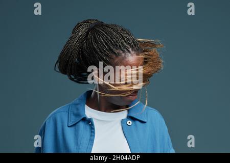 In-Motion-Porträt einer zeitgenössischen afroamerikanischen Frau, die vor blauem Hintergrund tanzt oder den Kopf schüttelt, mit afroamerikanischen Zöpfen im Fokus, Raum kopieren Stockfoto