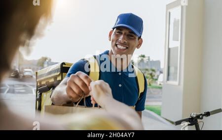 Hispanische Lieferer liefert Fast Food mit Elektroroller - liefern Kundendienst Stockfoto