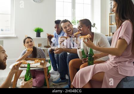 Eine Gruppe glücklicher junger Freunde, die Pizza genießen, Bier trinken, lachen und Spaß haben Stockfoto