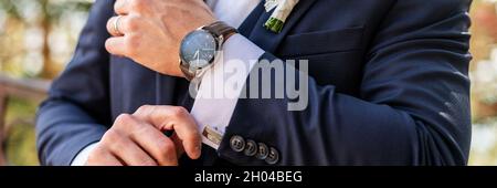 Bräutigam fixiert seine Manschettenknöpfe. Hübscher Bräutigam in dunkelblauem Anzug, der sich für die Hochzeit vorbereitet. Eleganter Bräutigam Hochzeitsmode. Stockfoto