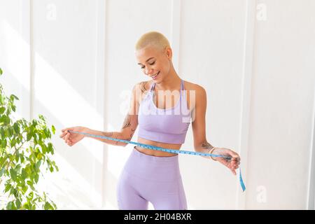 Gewichtsverlust Konzept. Aufgeregt fit Dame Messung ihre Taille und Blick auf Band mit Lächeln, Copy Space. Schlanke Frau glücklich mit ihrem Körper. Gesundes Livestyl Stockfoto