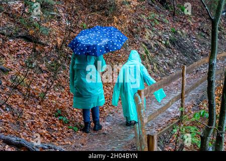 Frau mit Kindern auf Regenmänteln, die auf einem eisbedeckten Weg um den von Eis bedeckten See Synevyr, die Karpaten, Ukraine, wandern Stockfoto