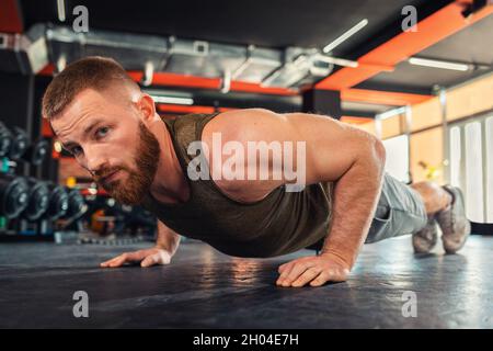Porträt eines jungen bärtigen, athletischen Mannes, der Liegestütze im Fitnessstudio macht. Nahaufnahme. Das Konzept von Fitness und Training. Stockfoto