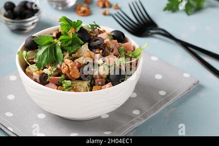 Salat mit Schinken, Ananas, schwarzen Oliven und Walnüssen in einer weißen Schüssel auf hellblauem Hintergrund. Stockfoto