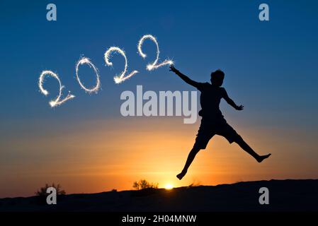 2022 geschrieben mit Funkeln, Silhouette eines Jungen, der in die Sonne springt, Neujahr-Karte Stockfoto