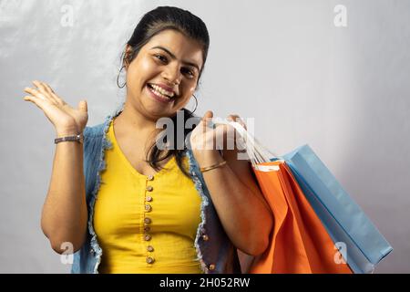 Eine schöne indische Frau in gelbem Kleid mit Einkaufstaschen und großem Lächeln auf weißem Hintergrund Stockfoto