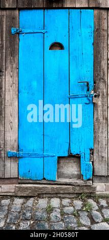 Alte verschlossene Schiefe blaue Türkisholztür aus drei alten Balken mit Vorhängeschloss, heller Eindruck Stockfoto