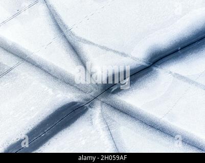 Luftdrohne Draufsicht auf schneebedeckten gefrorenen See oder Fluss Oberfläche mit großen rissigen Eis diagonalen Linien. Natürliche Winterlandschaft abstrakte Textur Stockfoto