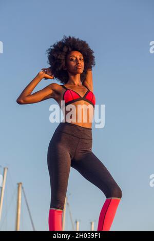 Junge athletische Frau in Sportkleidung, die sich mit einem blauen Himmel vor Hintergrund ausdehnt Stockfoto