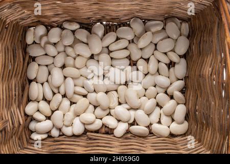 Getrocknete Körner von Bio-weißen Bohnen in einem Korb von Reben, Draufsicht. Stockfoto