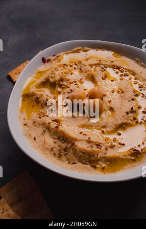 Kichererbsen-Hummus mit Olivenöl und geröstetem Sesam auf dunklem Hintergrund und selektivem Fokus. Stockfoto