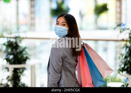 Einkaufen während der Coronavirus-Epidemie Konzept. Junge asiatische Dame in Gesichtsmaske hält Einkaufstaschen und posiert im Supermarkt. Tausendjährige Frau trägt Anti Stockfoto